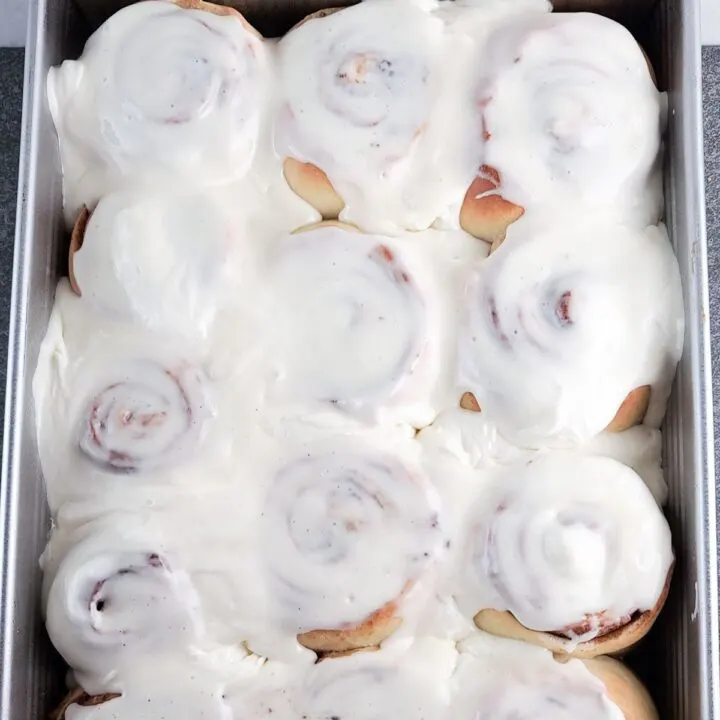 A rectangular pan of baked cinnamon rolls slathered with a lot of cream cheese frosting.