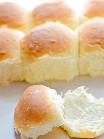 Baked homemade yeast rolls with one in front split in half with butter on one side