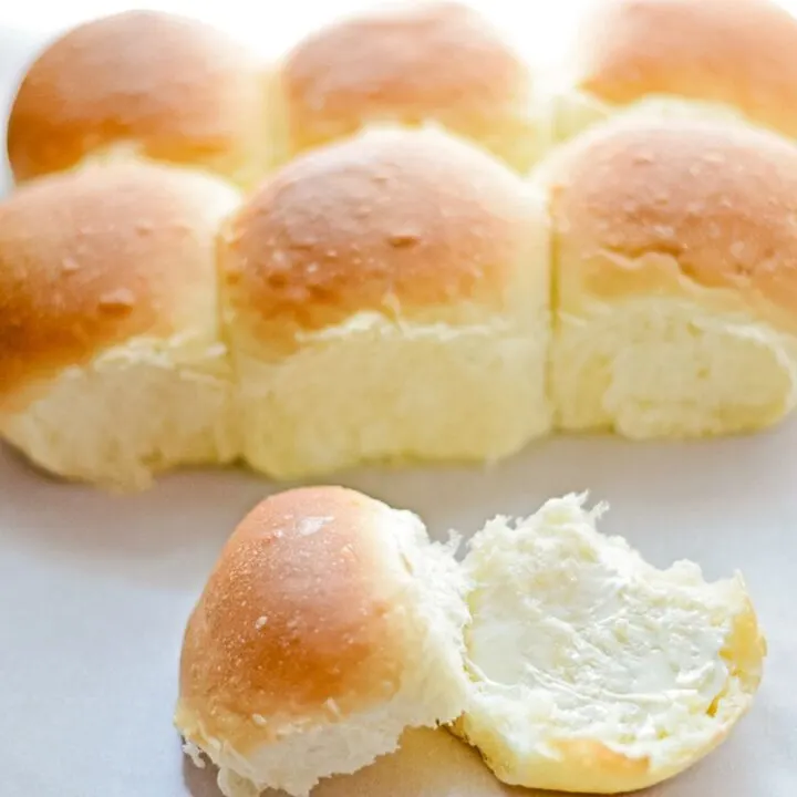 Baked homemade yeast rolls with one in front split in half with butter on one side