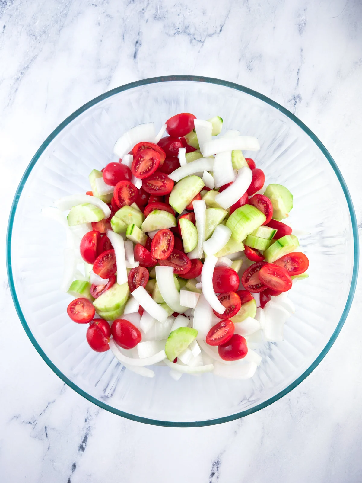 Sliced onion, tomato, and cucumber in a glass mixing bowl