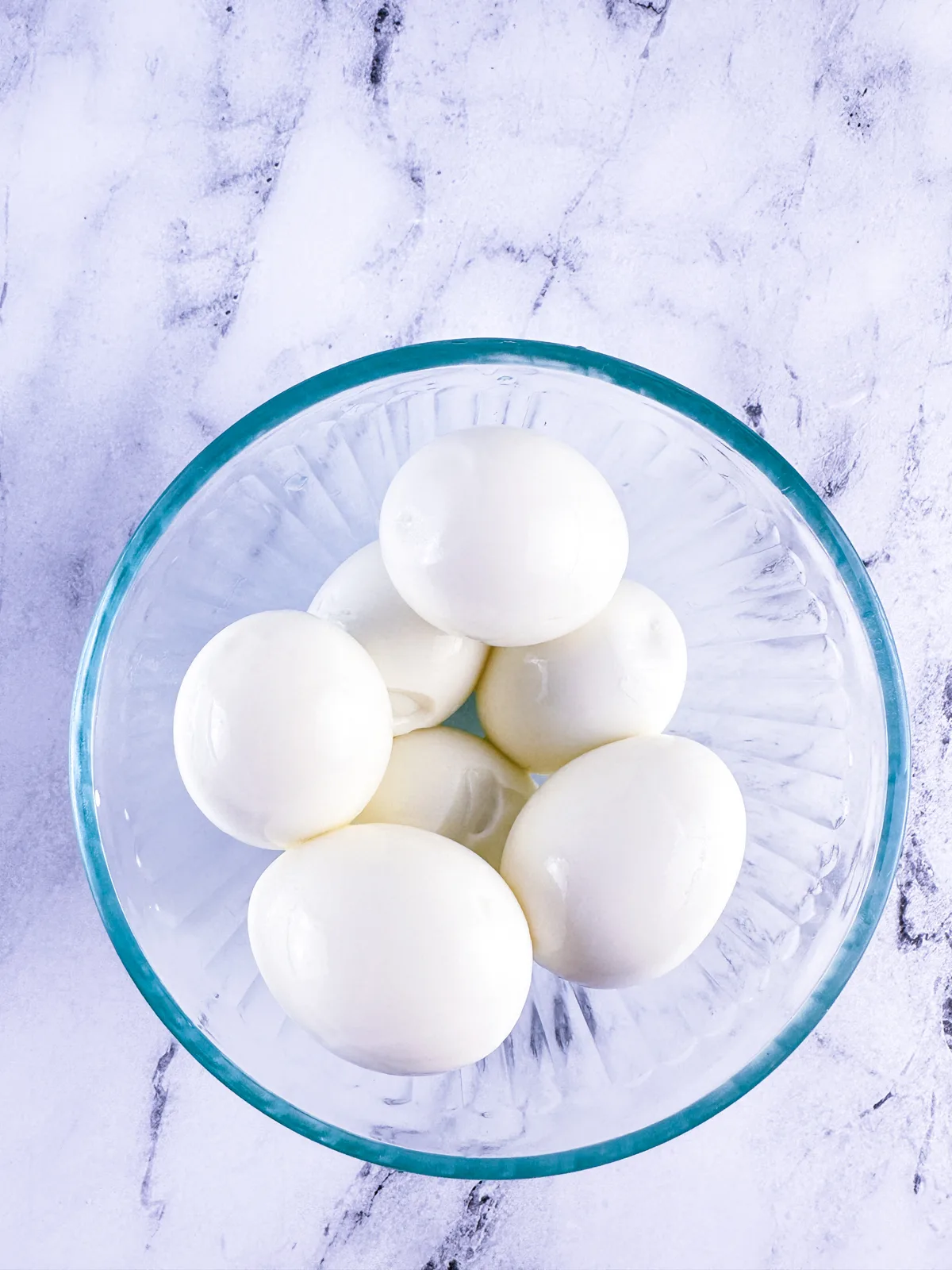 Peeled hard boiled eggs in a glass bowl.