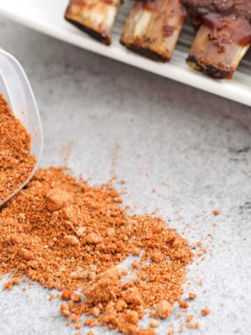 Pork rub in a container with prepared ribs in the background