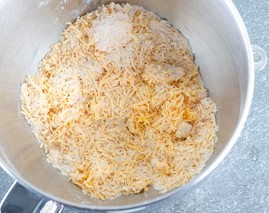 Shredded cheddar mixed into the flour and spice mixture in a stand mixer bowl.
