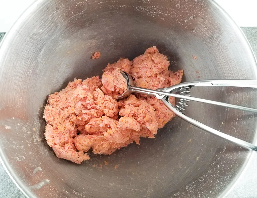 All the sausage ball ingredients mixed together in a mixing bowl with a scoop to start forming the balls.