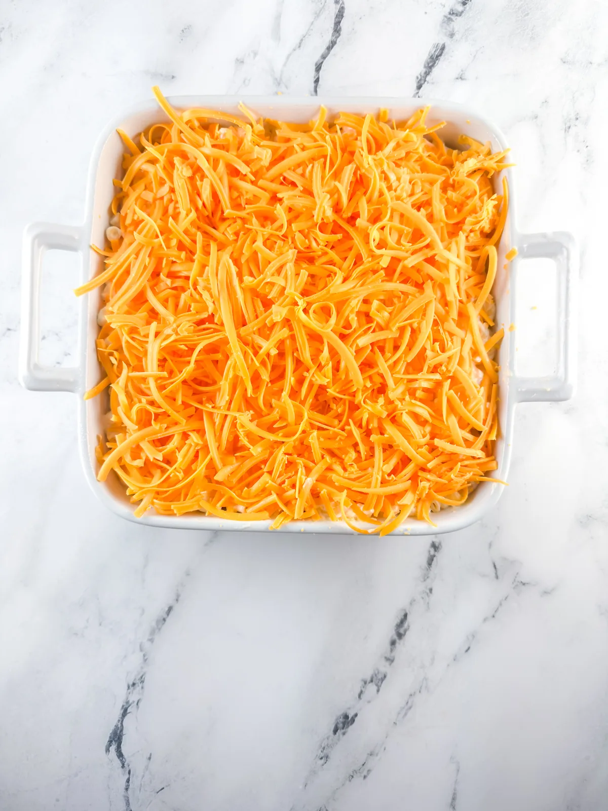 Unbaked macaroni and cheese covered with a layer of shredded cheddar before baking.