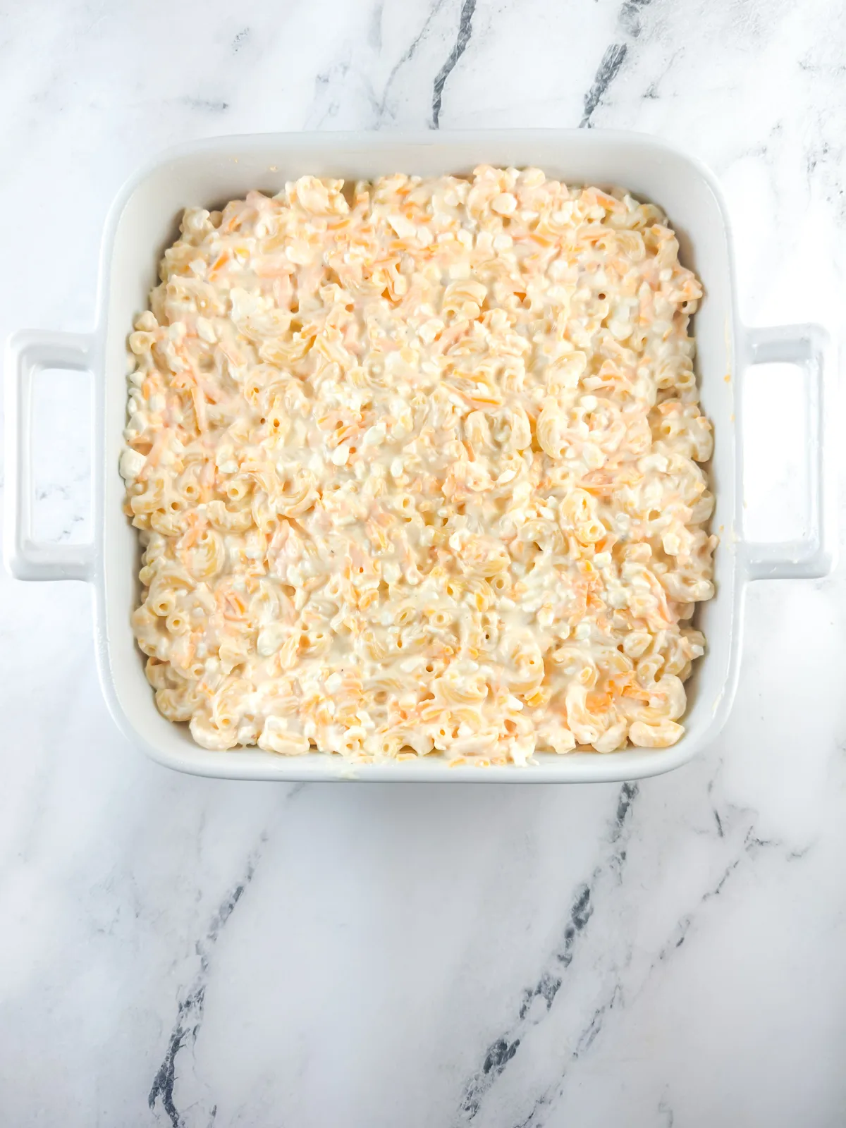 Unbaked macaroni and cheese in a square white baking dish.