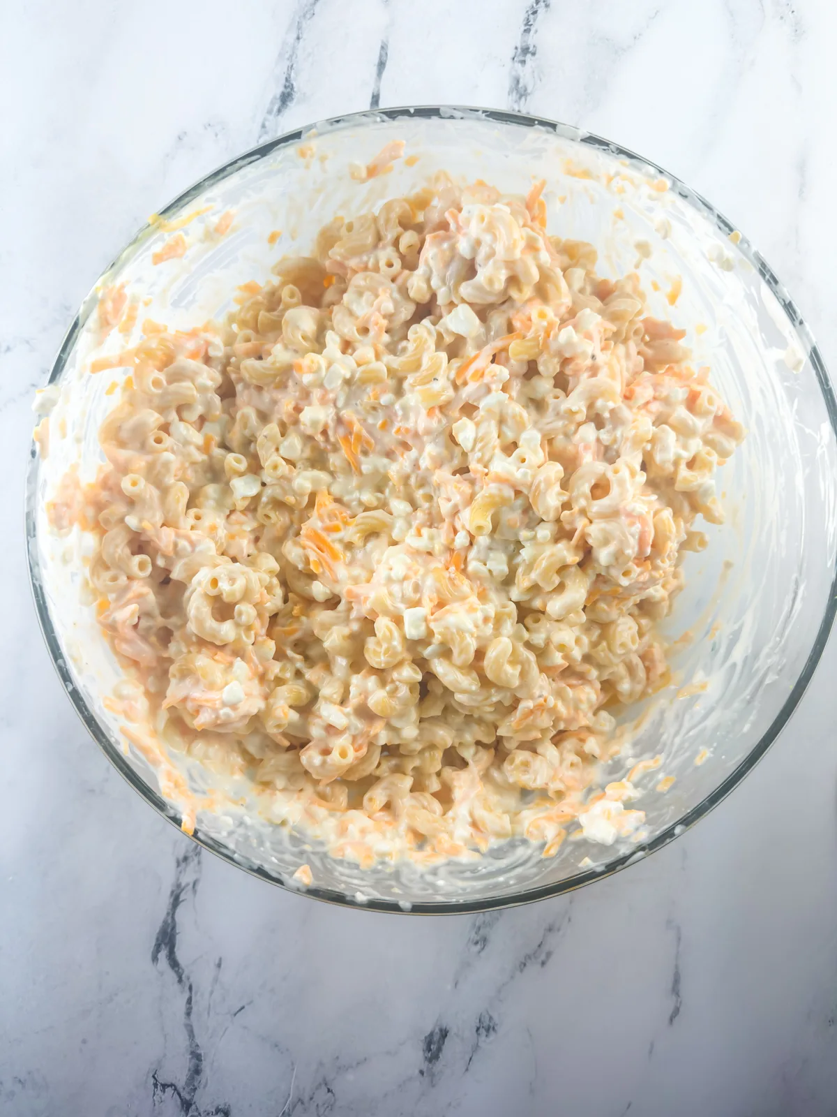 Baked macaroni and cheese ingredients mixed together in a large glass bowl.