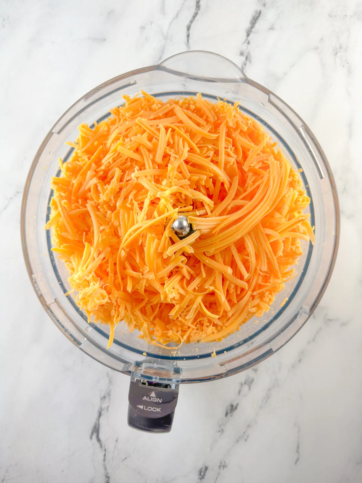 Shredded cheddar cheese in a food processor bowl.