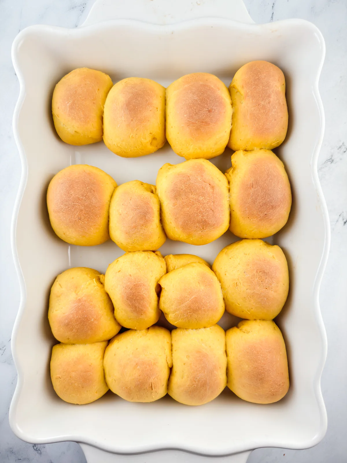 Baked pumpkin dinner rolls in a white baking dish.