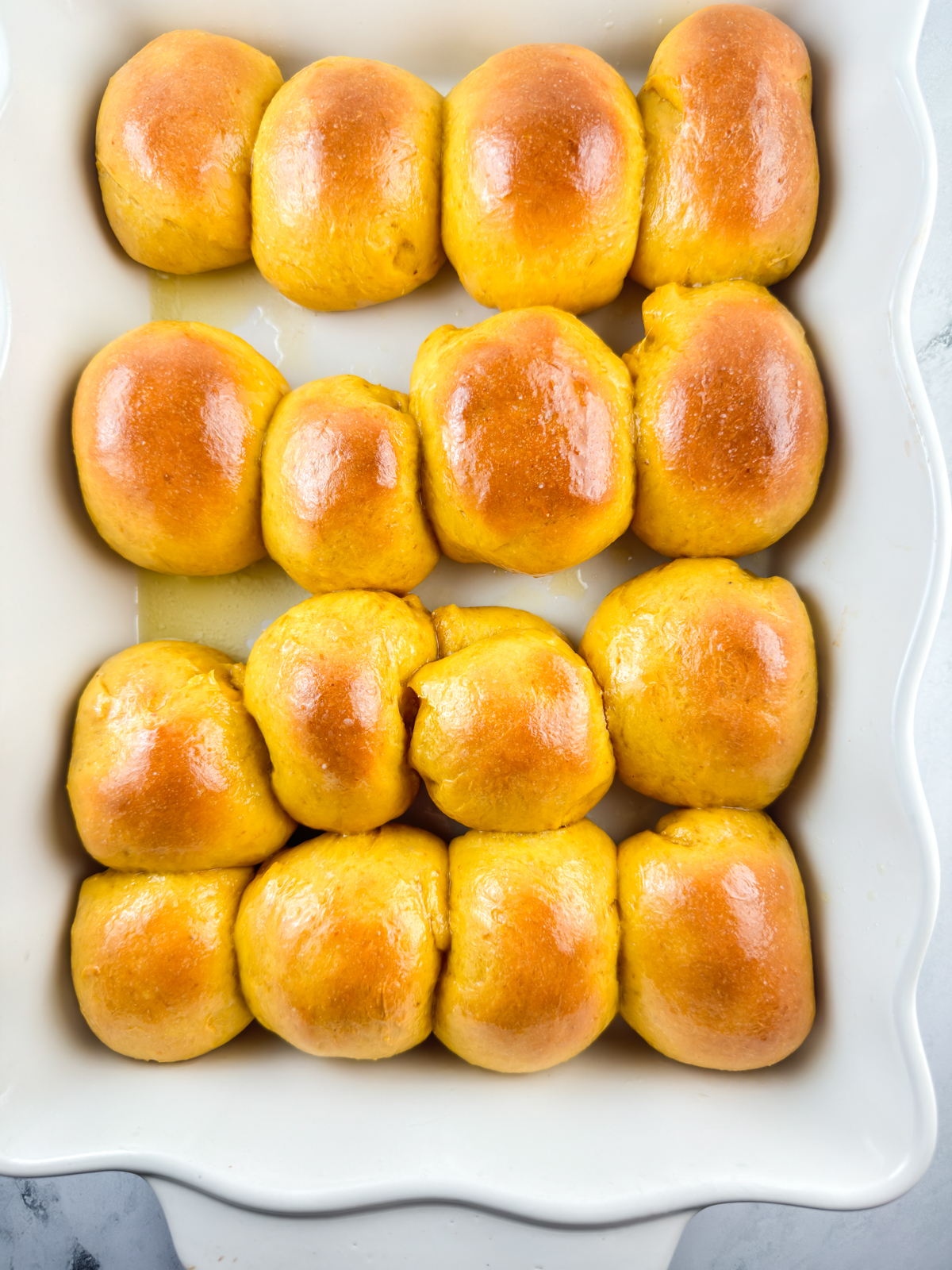 Baked pumpkin dinner rolls in a white baking dish that have been brushed with melted butter.