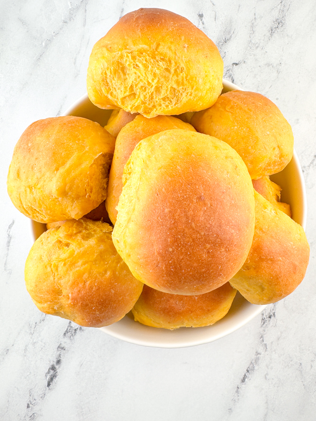 Baked pumpkin yeast rolls piled up in a white bowl.