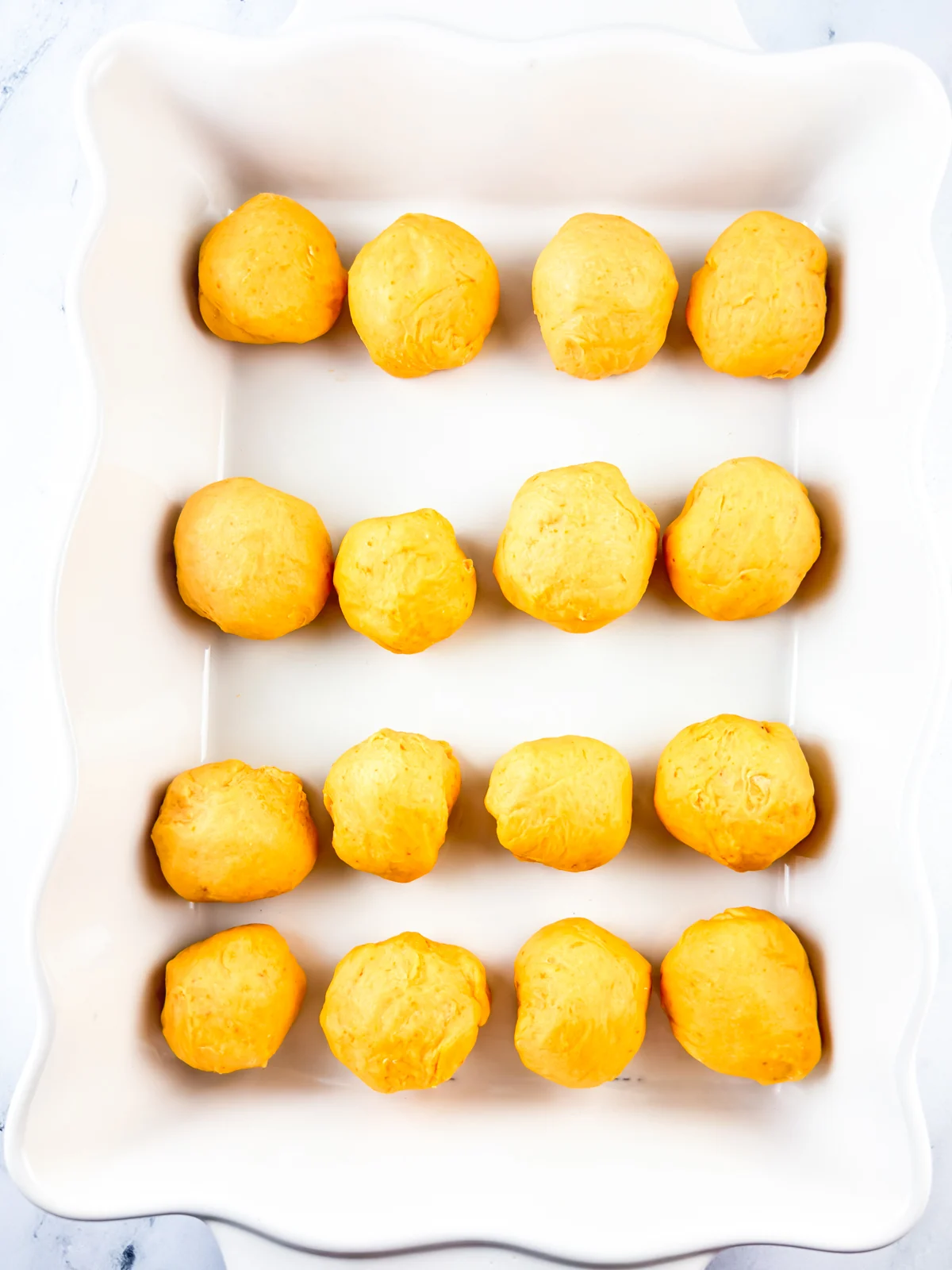 Rolled dinner rolls in white baking dish ready to rise.