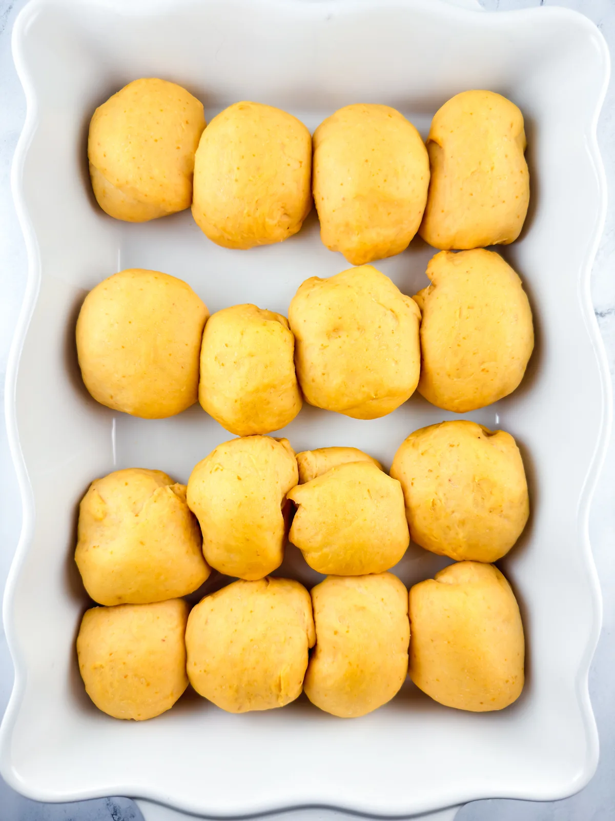 Pumpkin dinner rolls in white baking dish after rising.