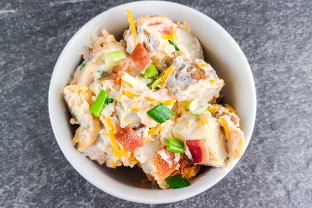 Overhead view of prepared baked potato salad garnishted with green onion, bacon, and shredded cheese.
