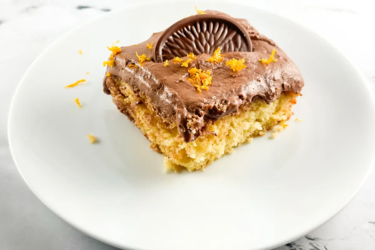 A piece of chocolate orange cake garnished with fresh orange zest and a slice of a Terry's Chocolate Orange.
